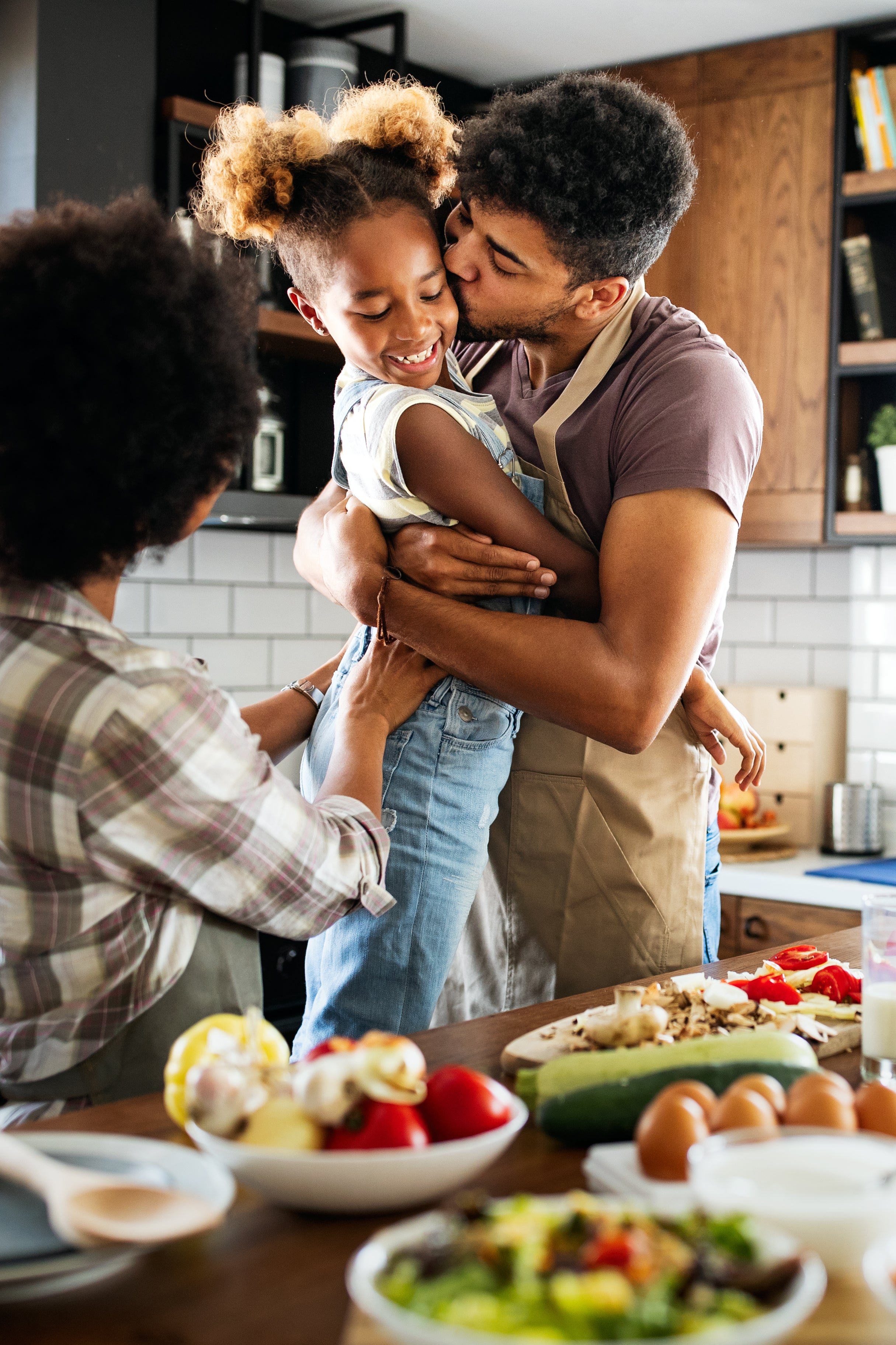 une-famille-cuisine-dans-la-cuisine-pendant-qu'un-père-étreint-et-embrasse-sa-fille-sur-la-joue