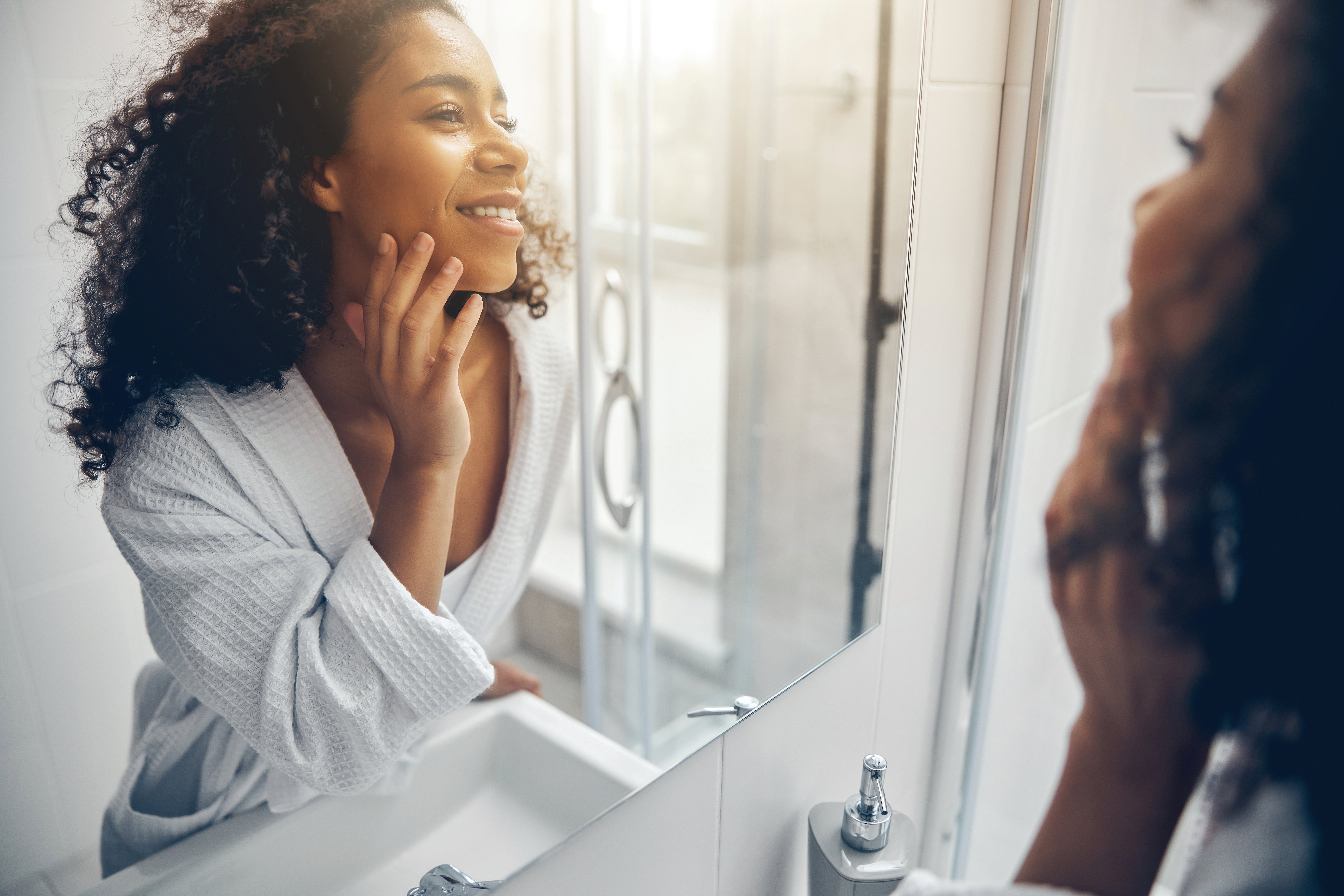 Femmes appliquant ses soins de la peau dans le miroir et souriant