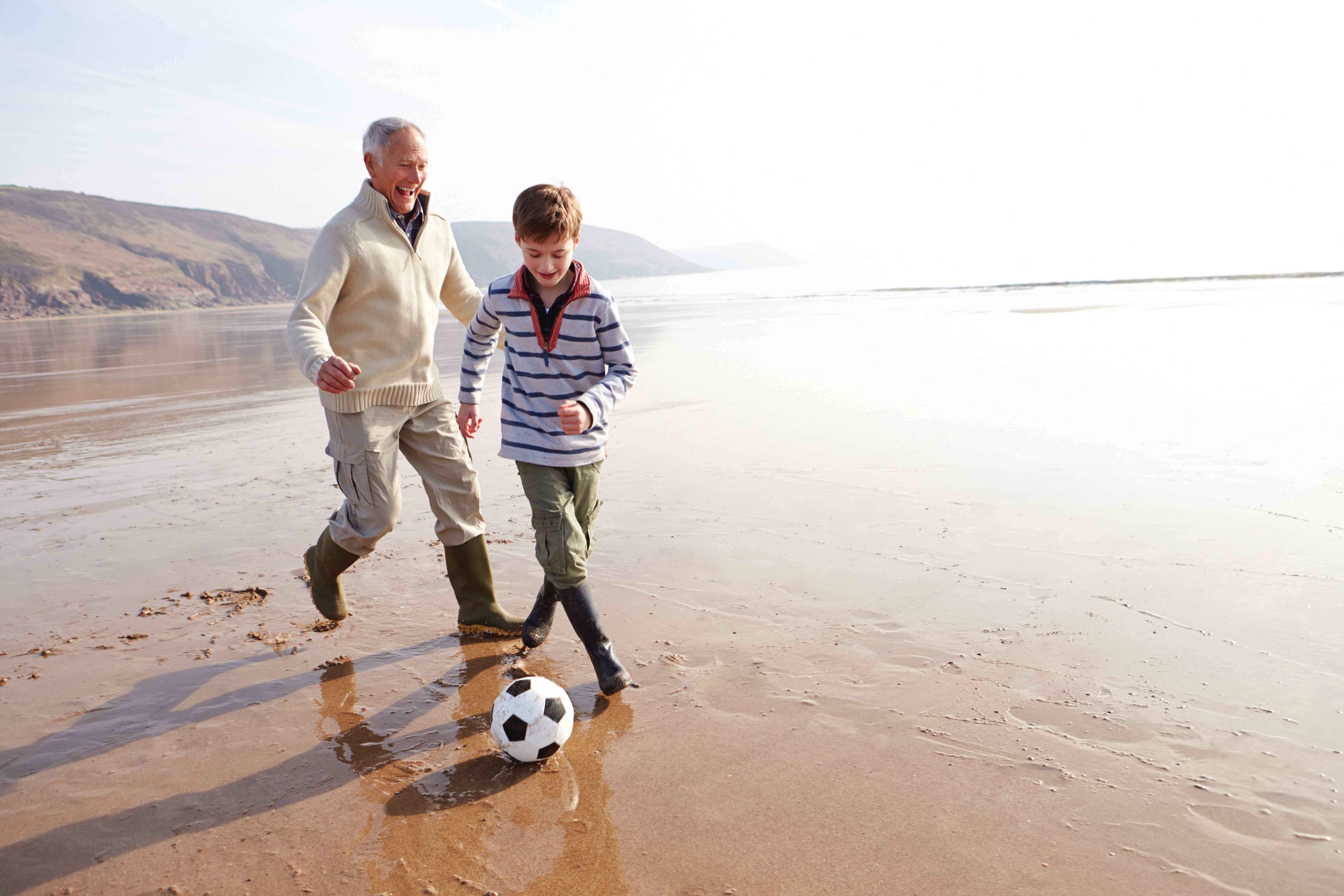 Grand-père jouant au football avec son petit-fils à la plage