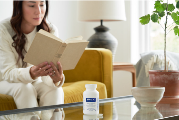 Une femme lisant un livre dans son salon avec une bouteille de supplément d'encapsulations pures sur sa table basse