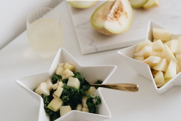 Un melon coupé sur un comptoir de cuisine à côté d'un verre d'eau et d'une salade de melon chou frisé.