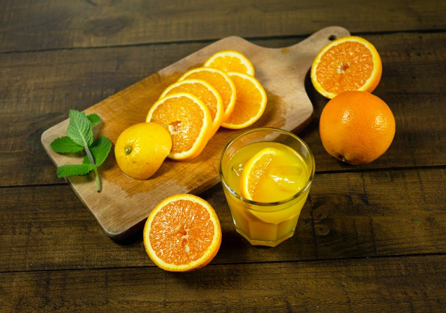  Oranges coupées sur une planche à découper en bois à côté d'un verre de jus d'orange frais.