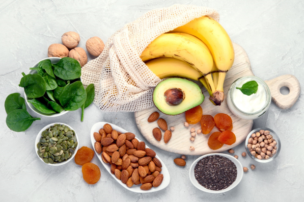 Bananas, apricot, almonds, seeds, spinach, yogurt all on a kitchen counter.