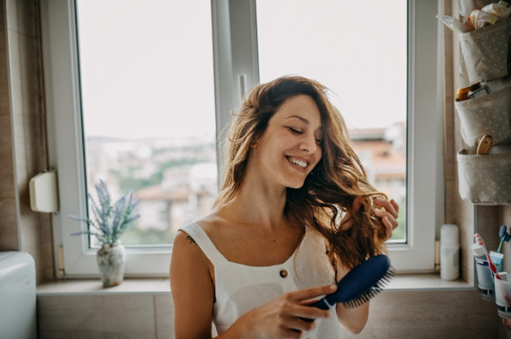 Women brushing her hair and smiling in the bathroom.