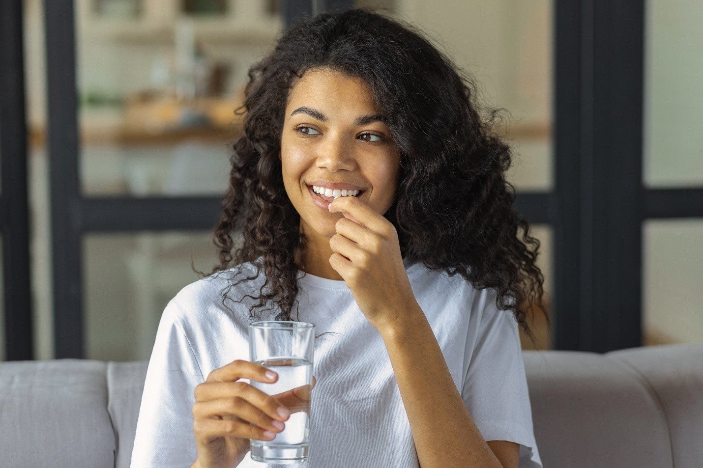 A women smiling and taking her daily vitamin supplement